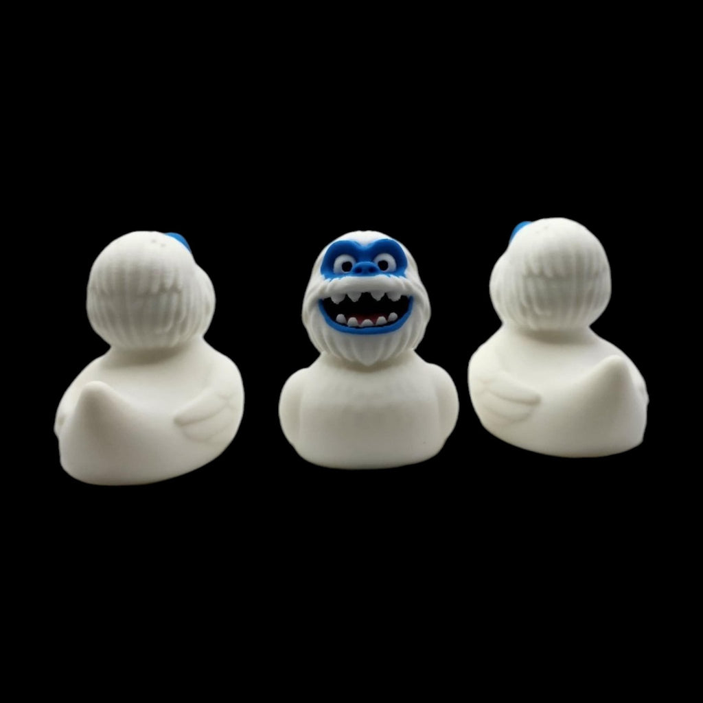 Front and angled side views of a white 3D printed Yeti duck with a blue face and toothy smile. - JM Designs