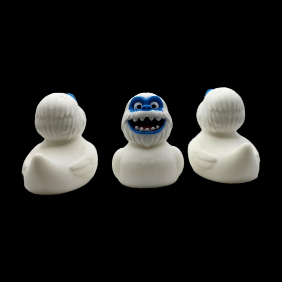Front and angled side views of a white 3D printed Yeti duck with a blue face and toothy smile. - JM Designs