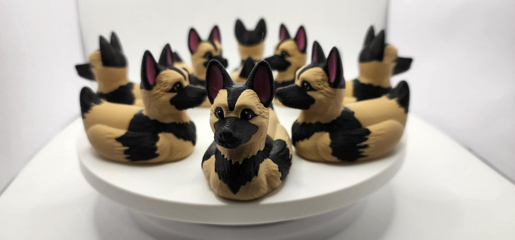 Close-up of a German Shepherd duck figurine with upright ears and a black muzzle against a gray background. JM Designs