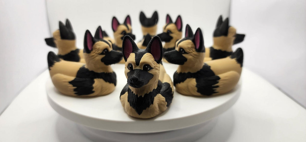Close-up of a German Shepherd duck figurine with upright ears and a black muzzle against a gray background. JM Designs
