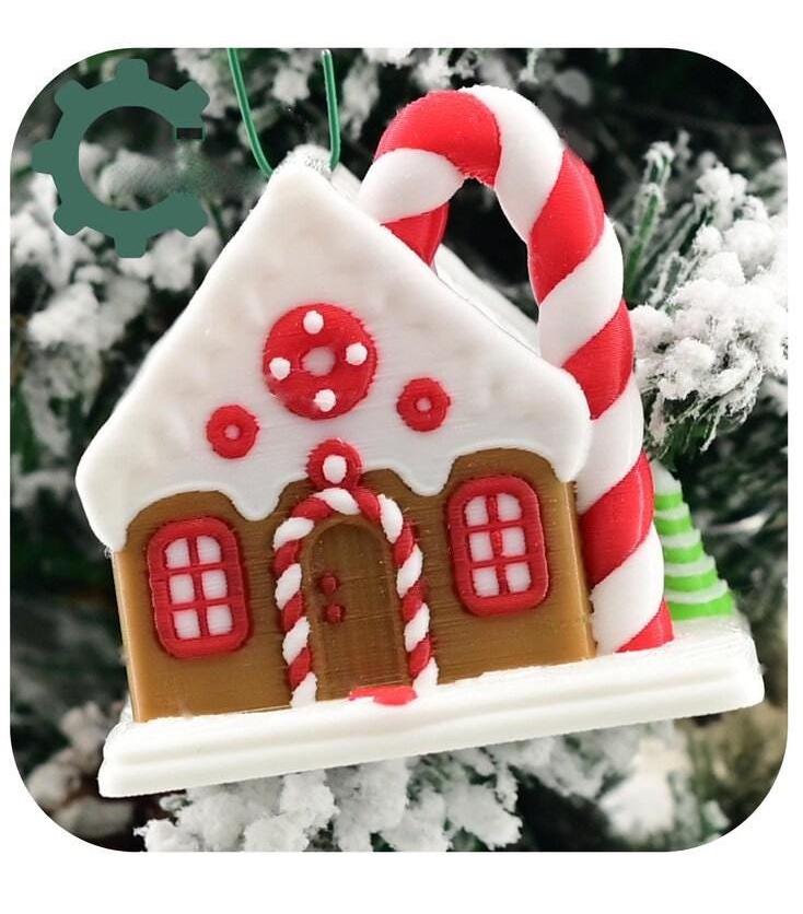 May include: Three gingerbread house ornaments hanging on a snowy Christmas tree. The ornaments are white, light blue, and green and yellow ombre. The ornaments are decorated with white icing and candy.