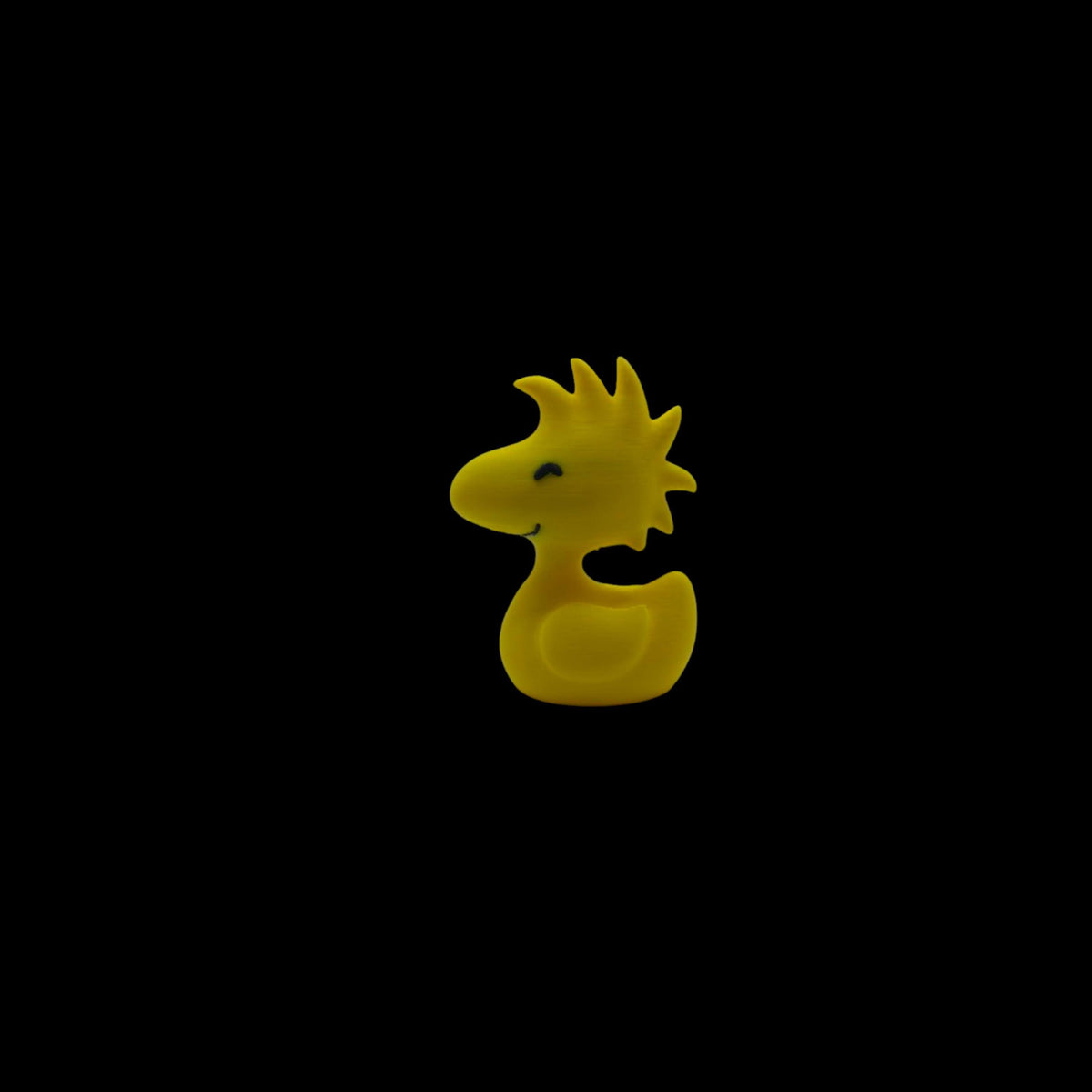 A yellow Woodstock figurine with spiky head feathers, a small beak, and two black dots for eyes, facing left.