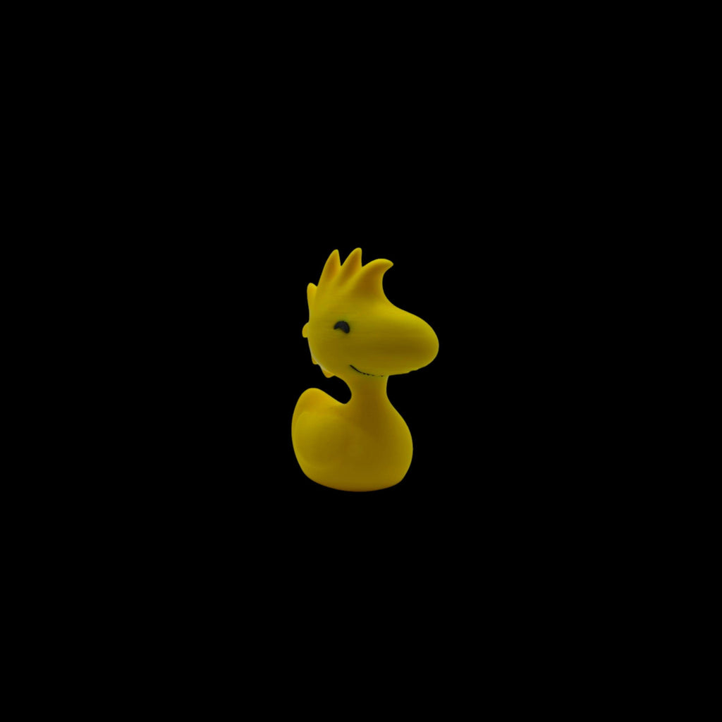 A yellow Woodstock figurine with spiky head feathers, a small beak, and two black dots for eyes, facing left.